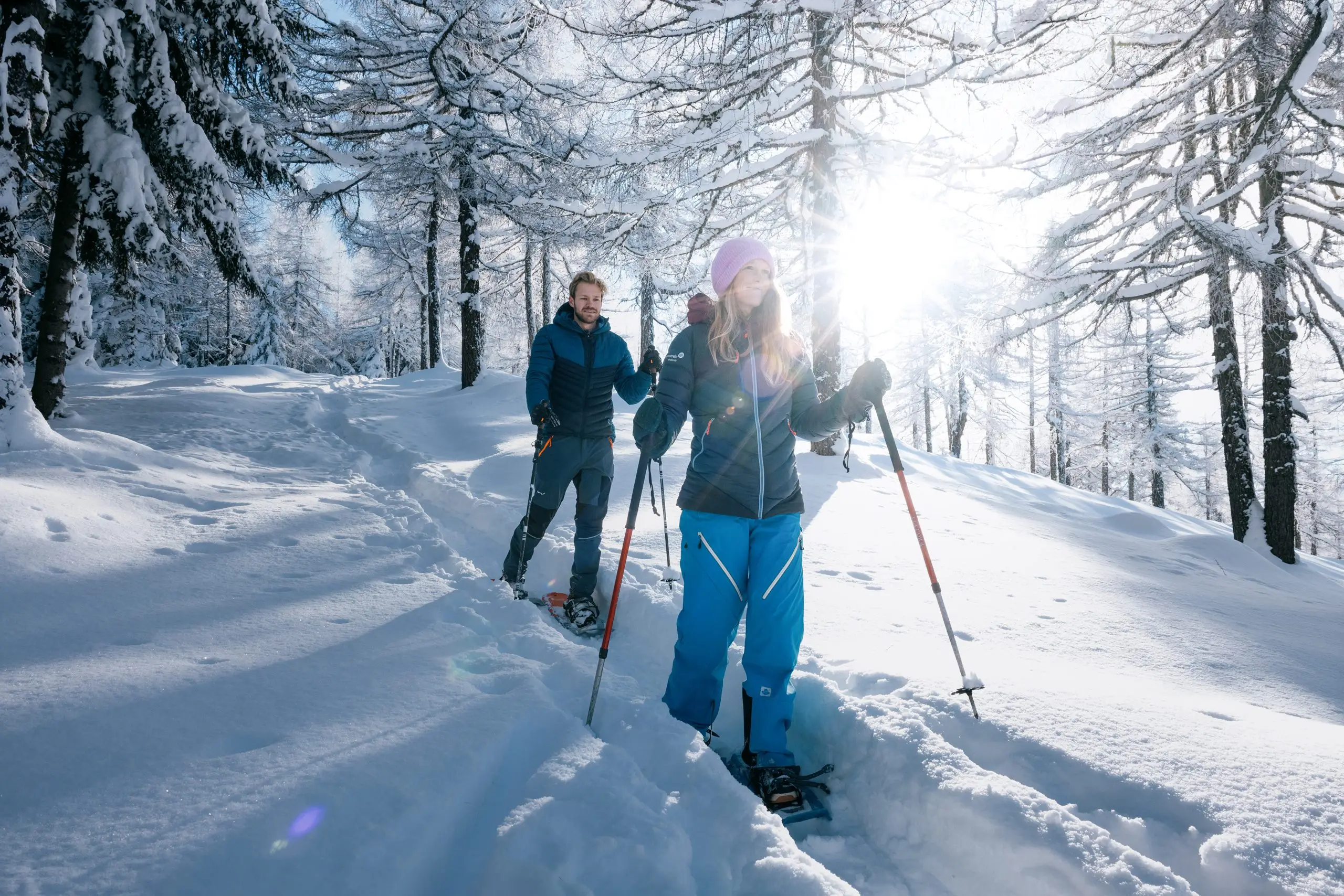 Zwei Winterwanderer auf verschneitem Weg zwischen schneebedeckten Bäumen